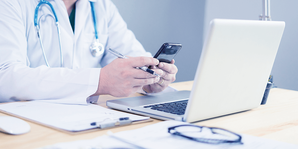 Clinician looking at data on paper notes, a mobile device and laptop